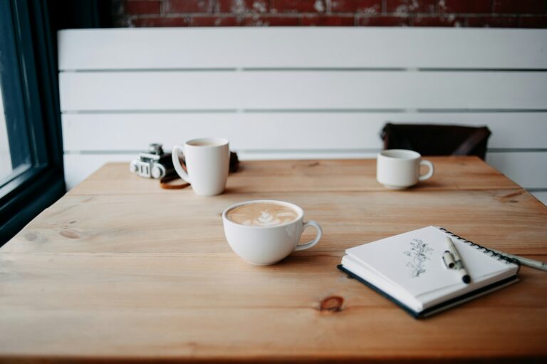 Coffee cups and a sketchbook on a café table, illustrating the fika meaning of a shared pause.