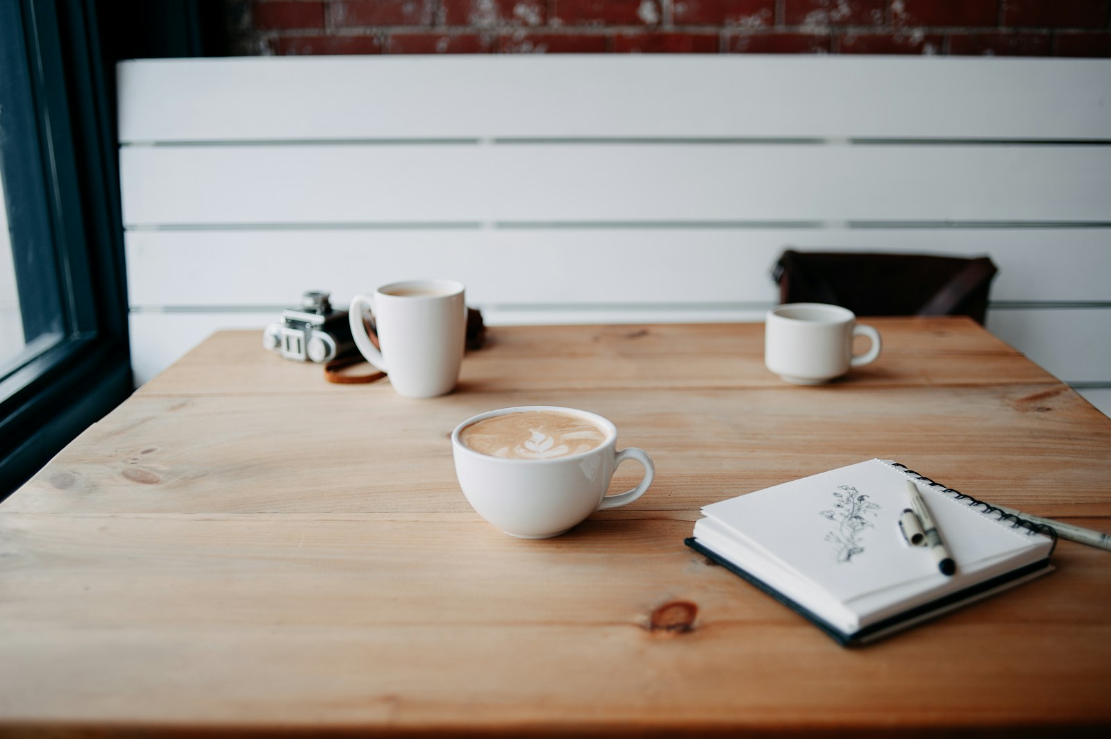 Coffee cups and a sketchbook on a café table, illustrating the fika meaning of a shared pause.